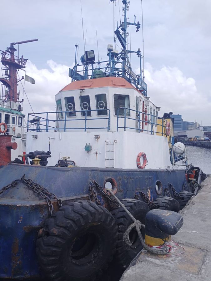 A tug moored alongside the quay with tyre fenders, port cranes behind
