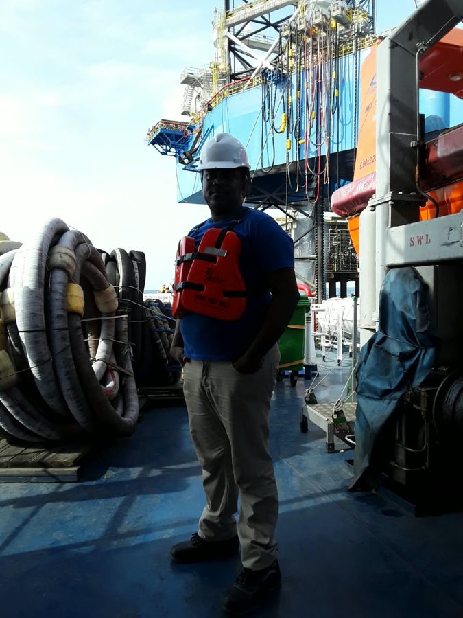 A crew member in a hard hat and life jacket on the deck of an offshore vessel