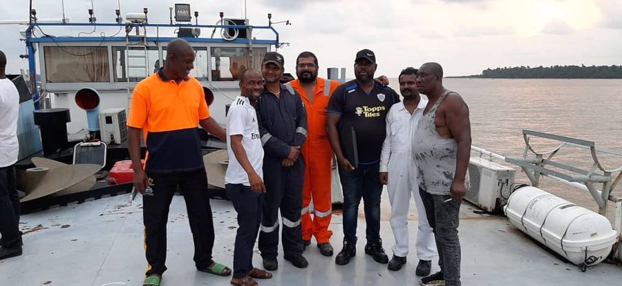 Team members standing on the deck of a vessel beside the river