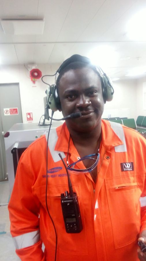 A crew member in orange coveralls wearing a headset and radio