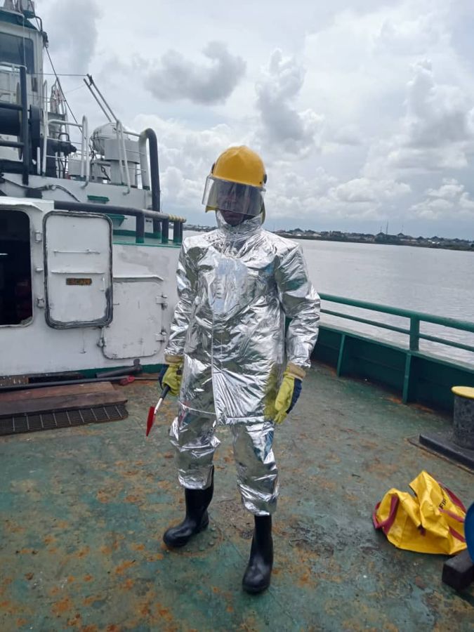 A crew member in a silver fire-protection suit and helmet on deck